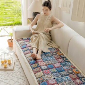 Woman sitting on a sofa with a colorful quilt, reading.